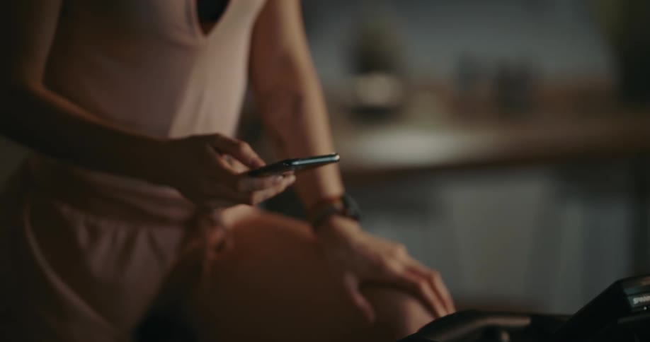 A woman puts in earbuds and scrolls through her phone while sitting on an exercise bike
