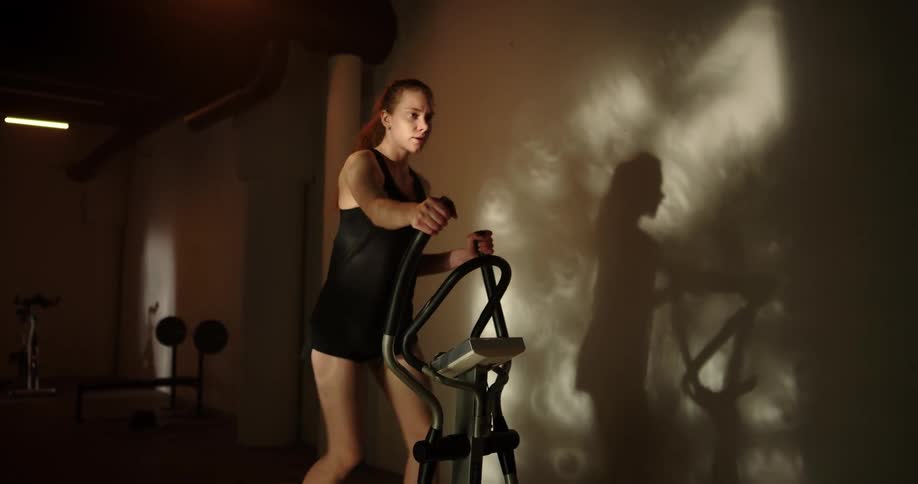 Woman with ponytail black top and shorts uses cross trainer in gym