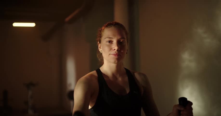 Woman with ponytail and black tank top uses cross trainer in gym
