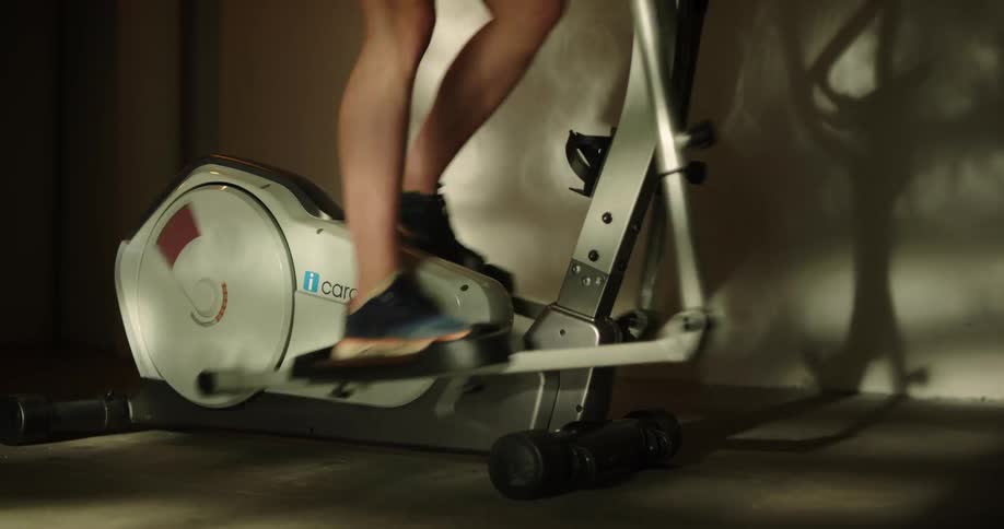 A woman is standing on an exercise machine and pedaling as she works out