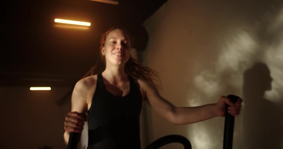 Determined woman with ponytail black top and shorts uses cross trainer at gym