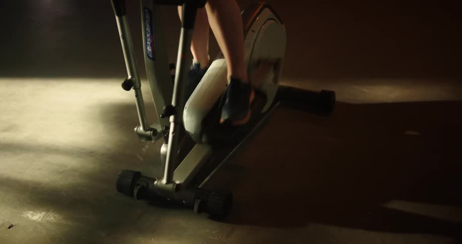 A womans feet and legs move as she ride an exercise machine