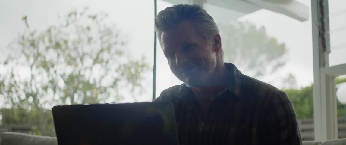 Man video calls using laptop while back lit and partially silhouetted