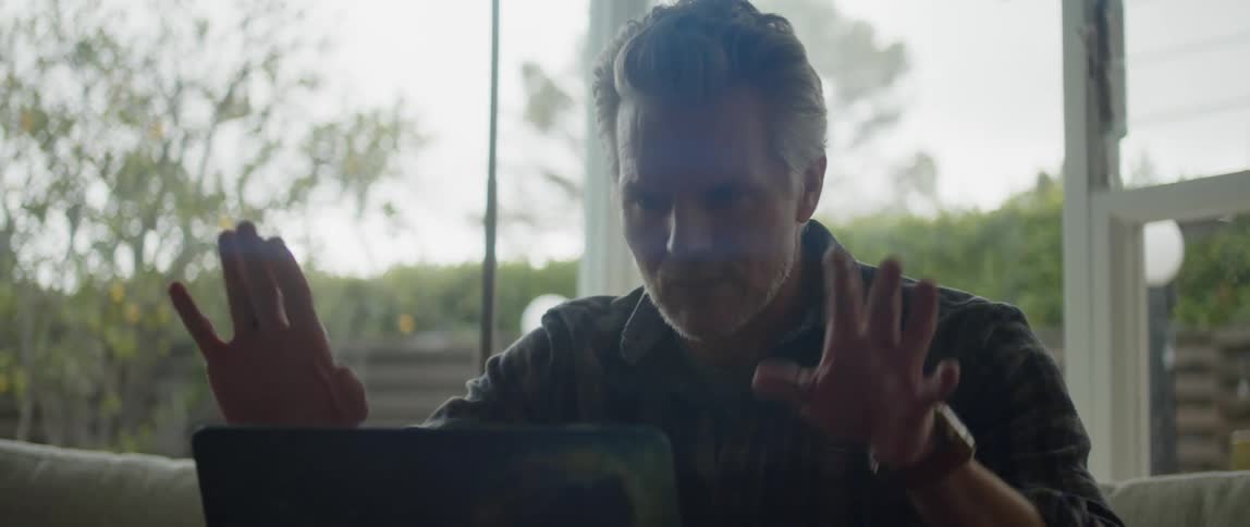 Man sits on couch gesturing while video conferencing via a laptop