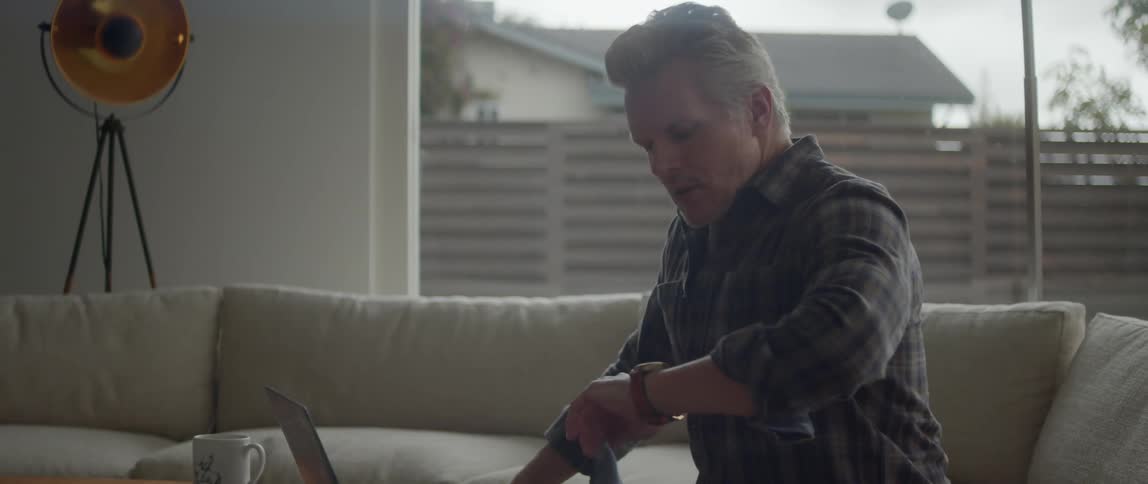 A man checks his watch by the laptop