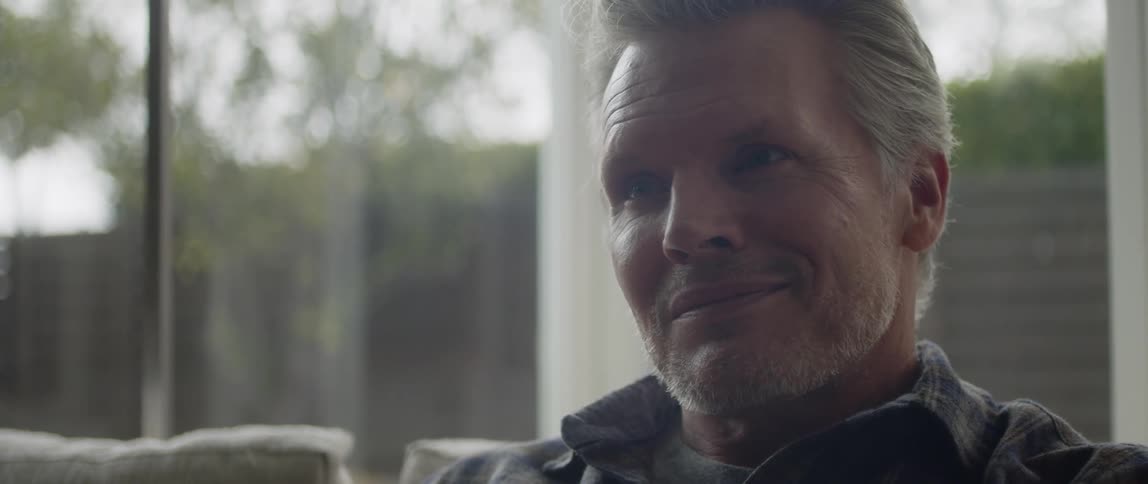 A man smiles while sitting on his couch