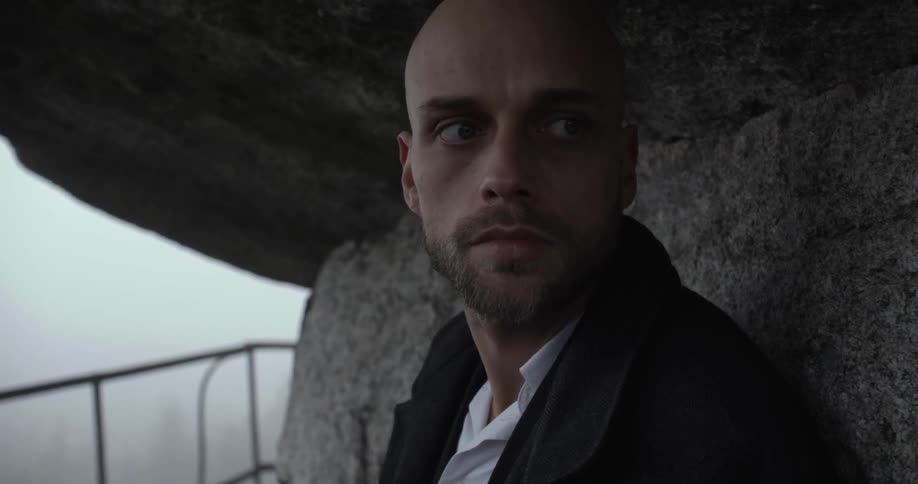 A man wearing a suit jacket stares outward with a foggy sky in the backward