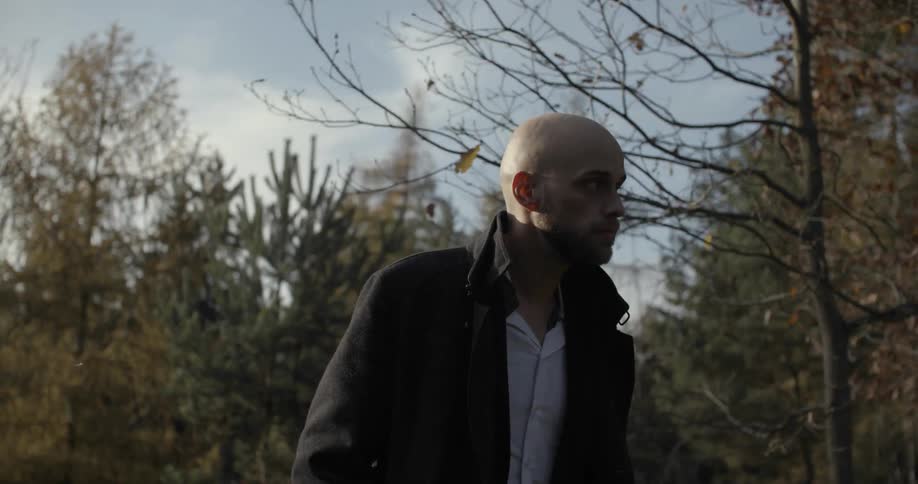 A bald man walks near some trees