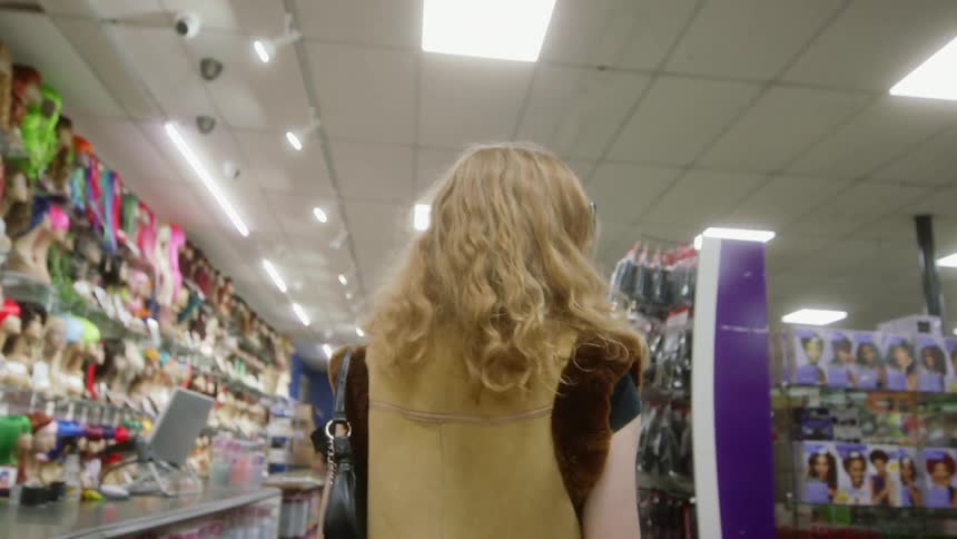 Blonde woman with sunglasses and yellow vest walks through variety store