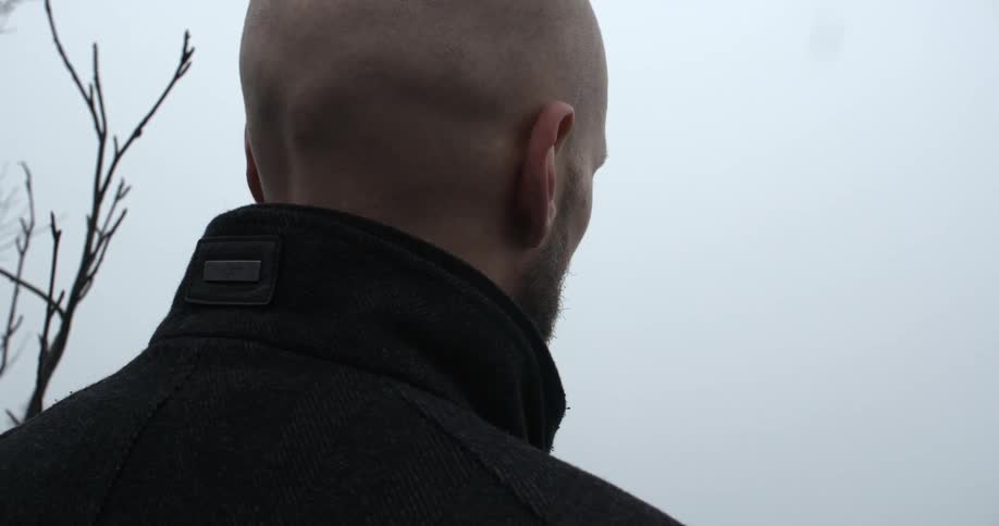 A bald-headed man stands staring into the distance