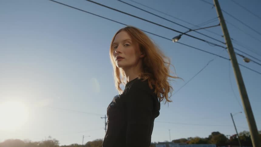 A woman poses as she stands under power lines