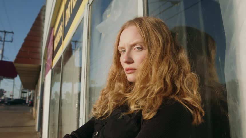 Woman leans against store window near street