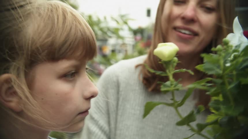 A mother and daughter smelling a potted flowering plant outside at a nursery