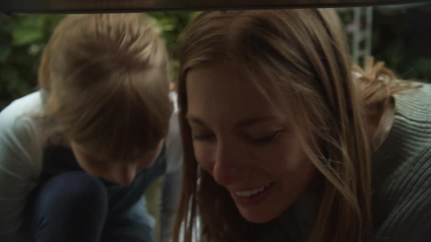 A mother and daughter take turns smelling a pink flower outdoors during the day