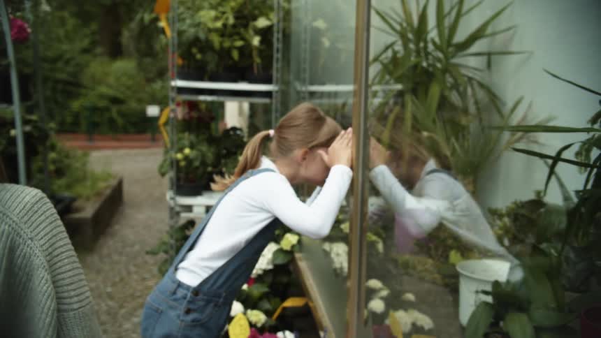 A mother and daughter are walking outdoors and looking at plants