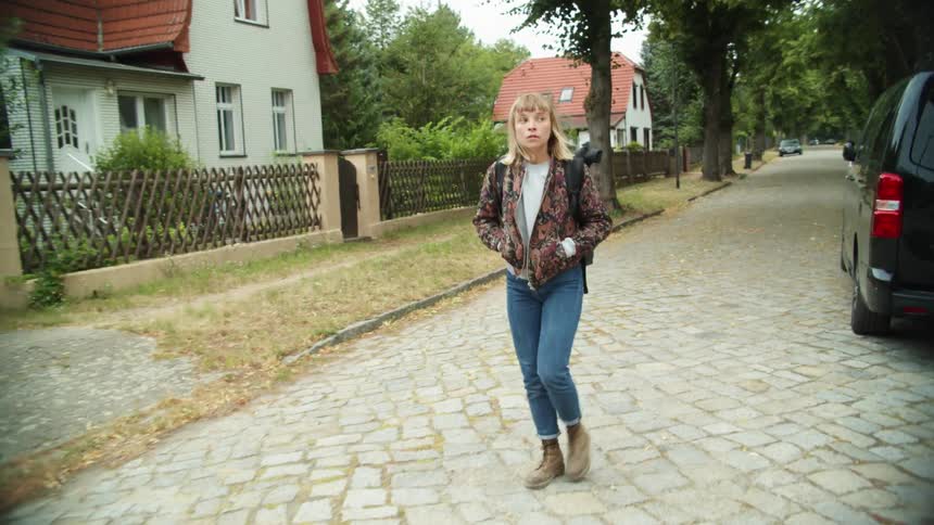 A teenage girl walking through a neighborhood while wearing a backpack