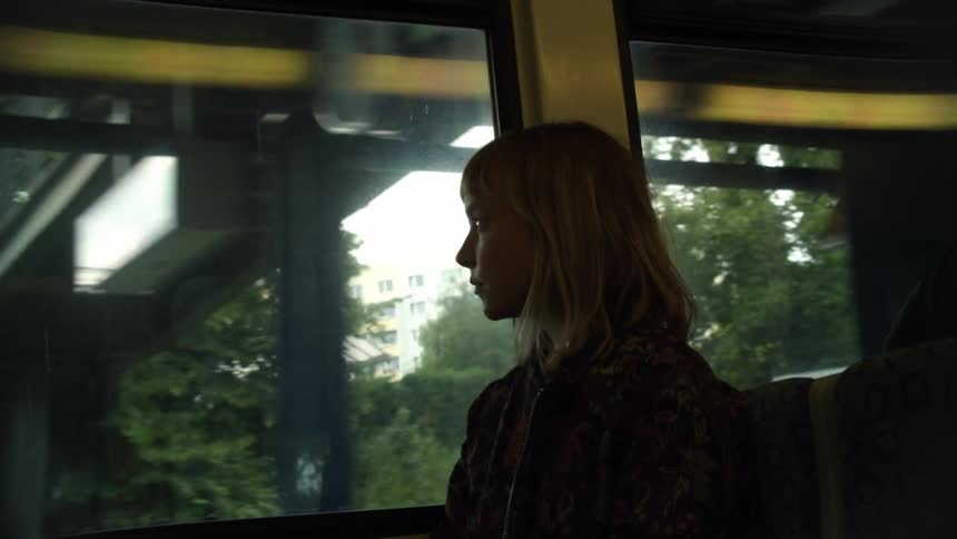 A woman is riding in the train and looking out the window
