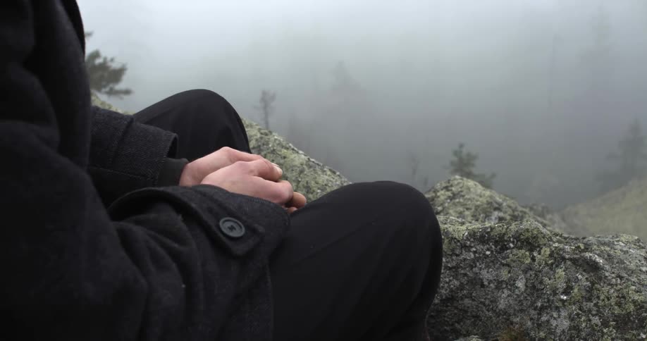 A man sitting on the side of a cliff on a foggy day