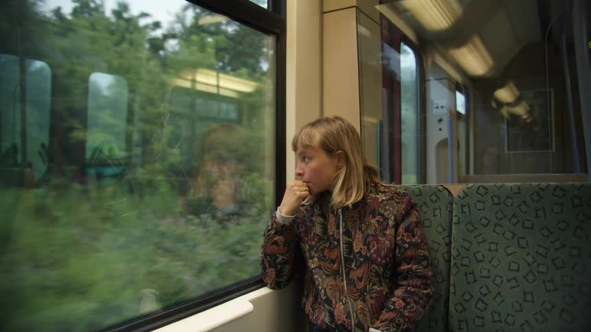 Young woman sitting in a train near the window looks outside pensively