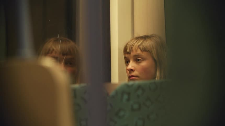 Young woman sitting in a moving train near the window looks outside pensively