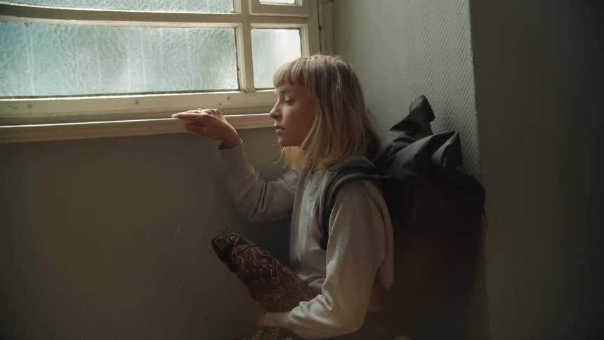 A woman sitting down next to a window indoors
