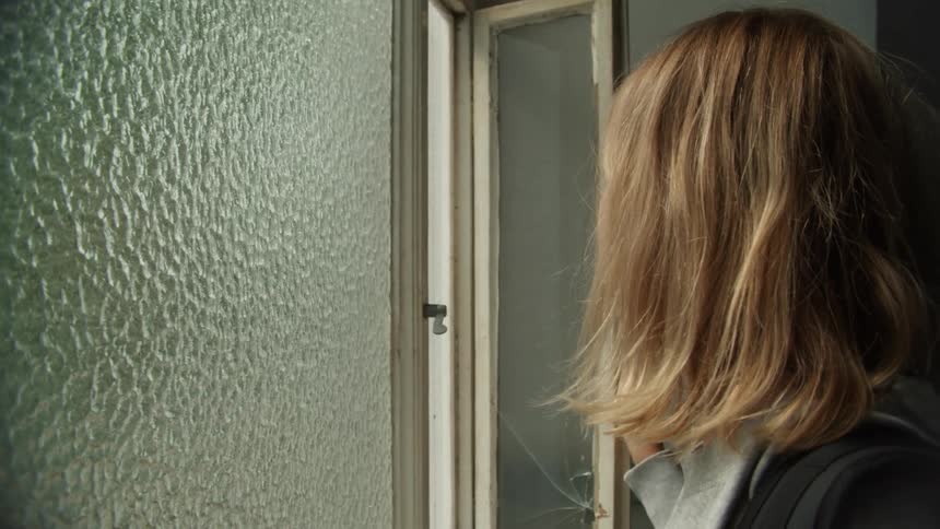 Blonde woman strokes glass before opening window and looking out
