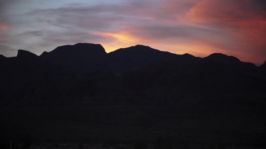 The sun setting behind mountains on a cloudy evening