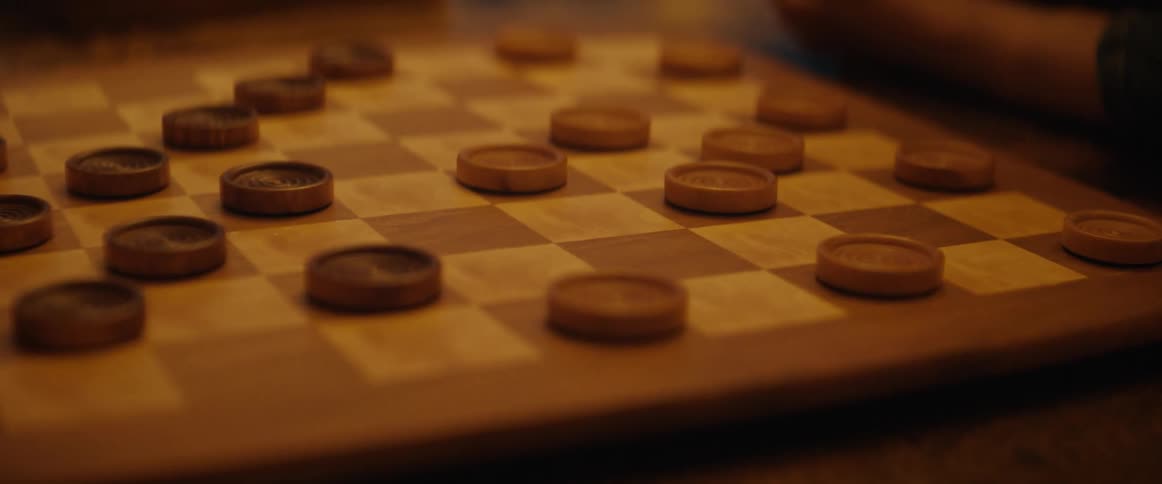 A child sitting next to a checkerboard moves a checker with her finger