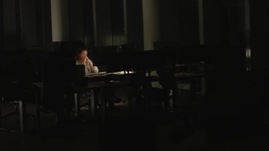 Woman sits alone in front on one of several computers in dark office