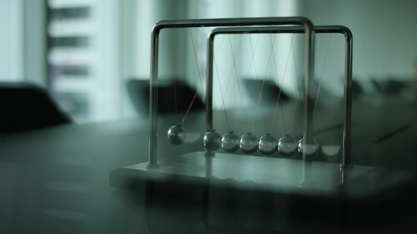 Silver balls are swinging and hitting each other in a newtons cradle sitting on a table