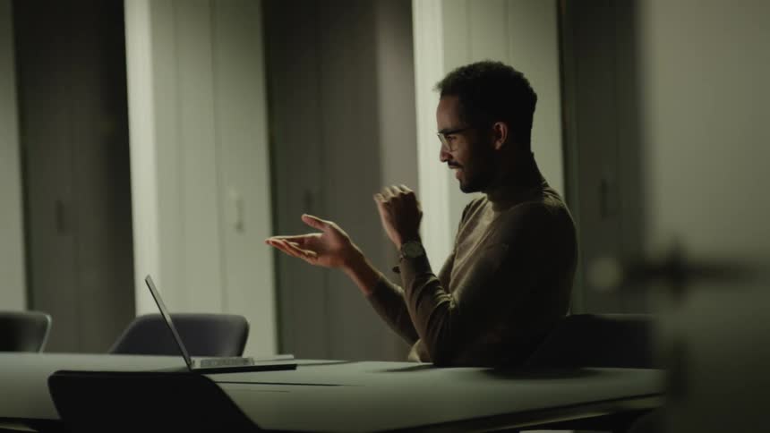 A man sits in an office and video chats on a laptop