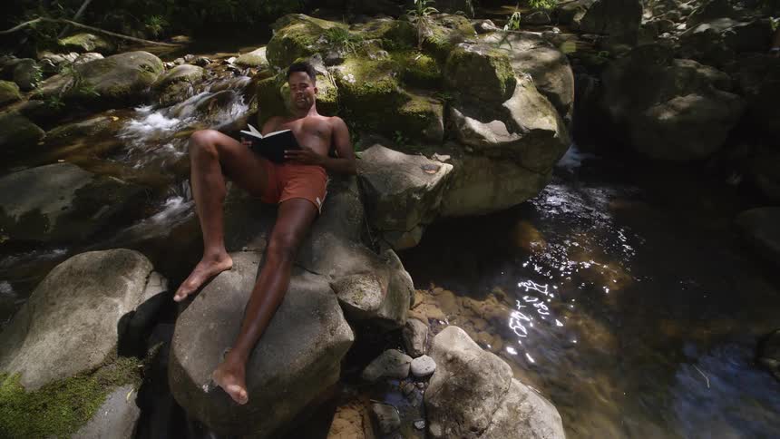 A man reads while lying on rocks along the river