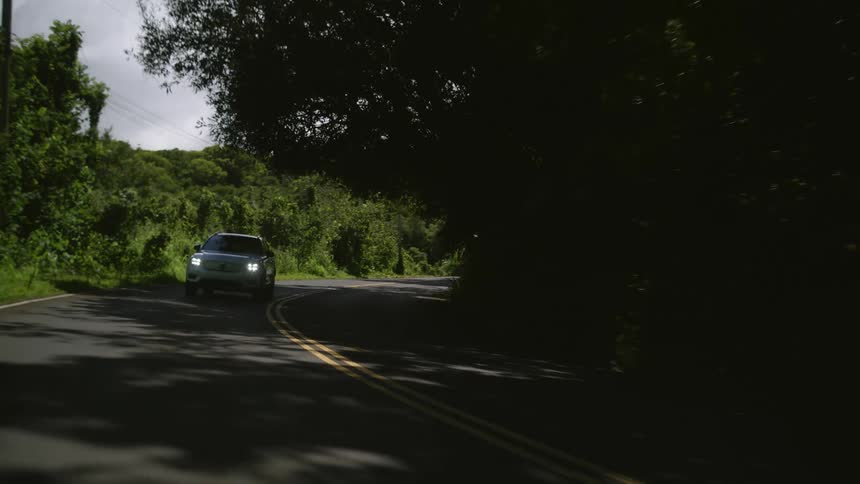 A car travels along a road through a forest on a cloudy day
