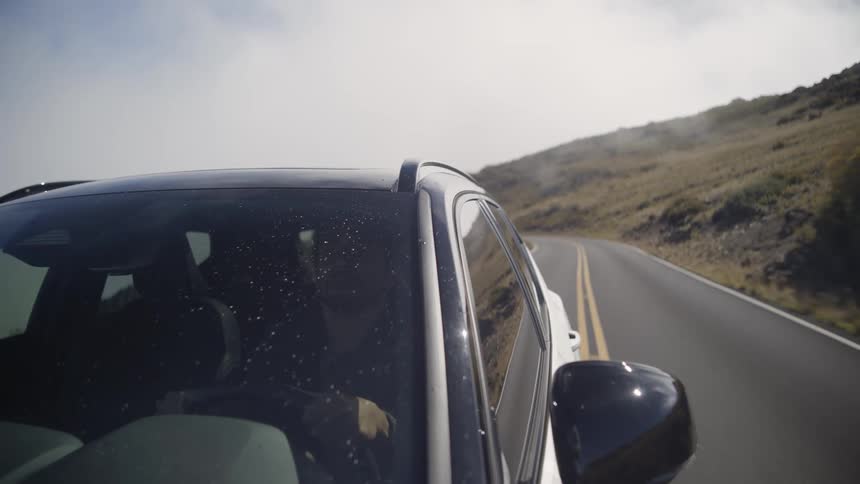 A man drives a car on a road along a hillside during the day