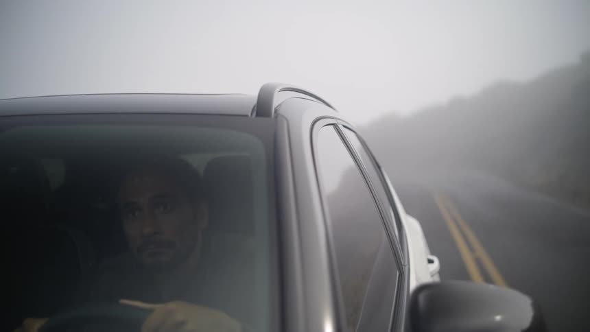 A man drives a car along a foggy countryside road on a cloudy day