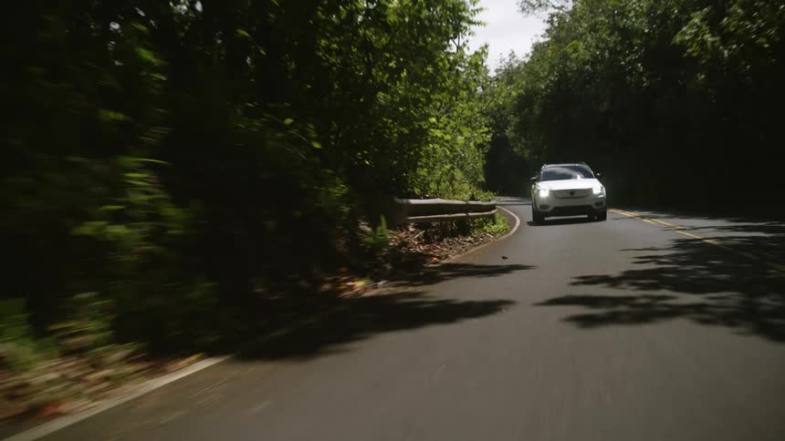 White car with headlights on driving on a road in the countryside at daytime