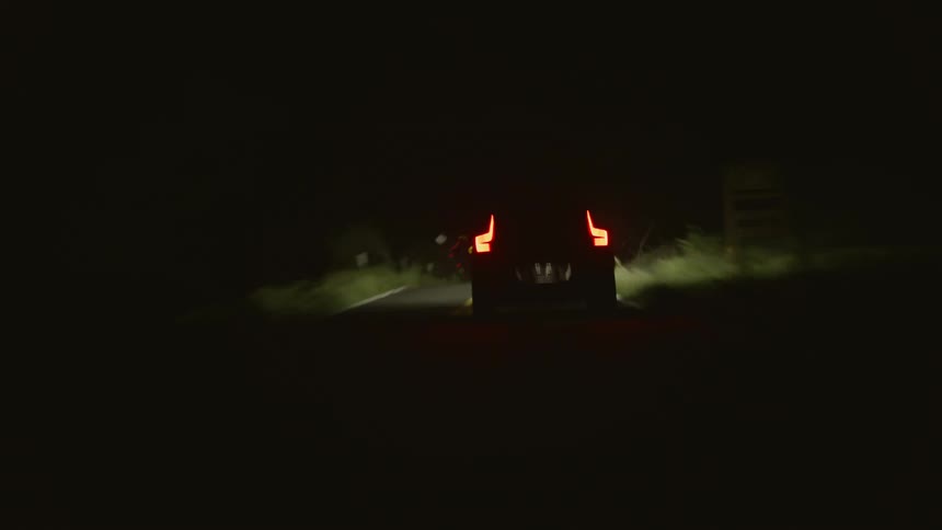 A vehicle speeds down a narrow road at night
