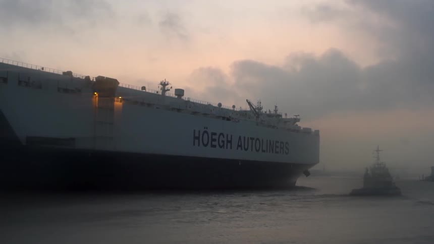 A tugboat leads a massive freighter out of a harbor
