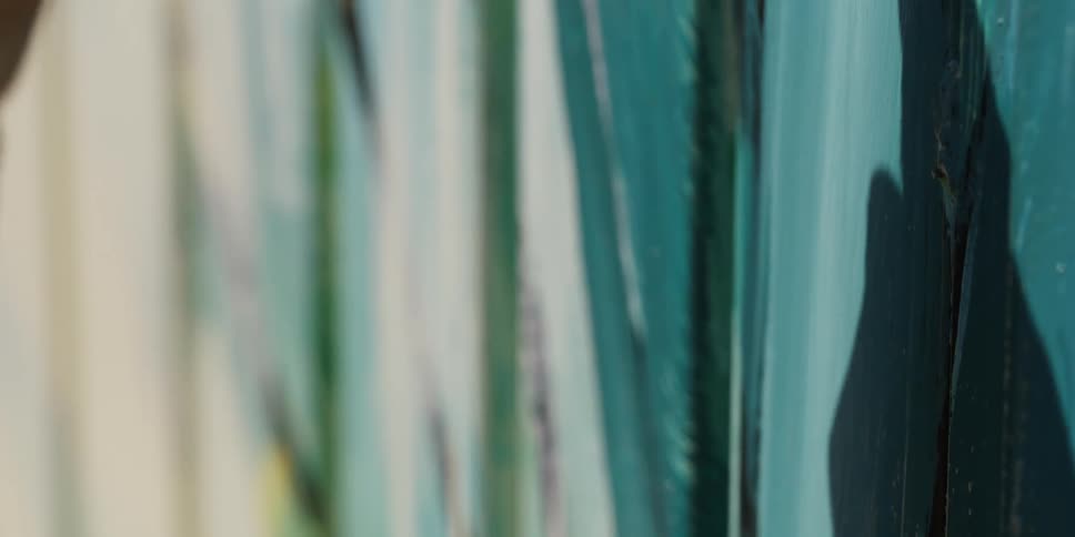 A man paints a colorful design on his picket fence