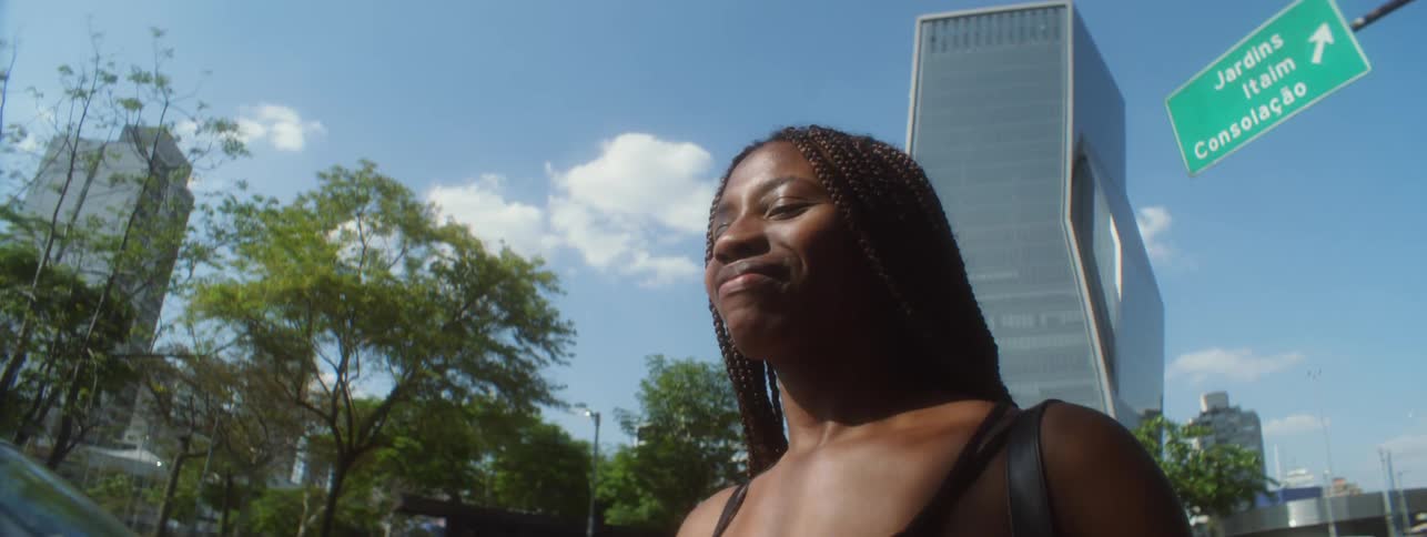 Woman smiles while walking along busy street near skyscraper with angular architecture