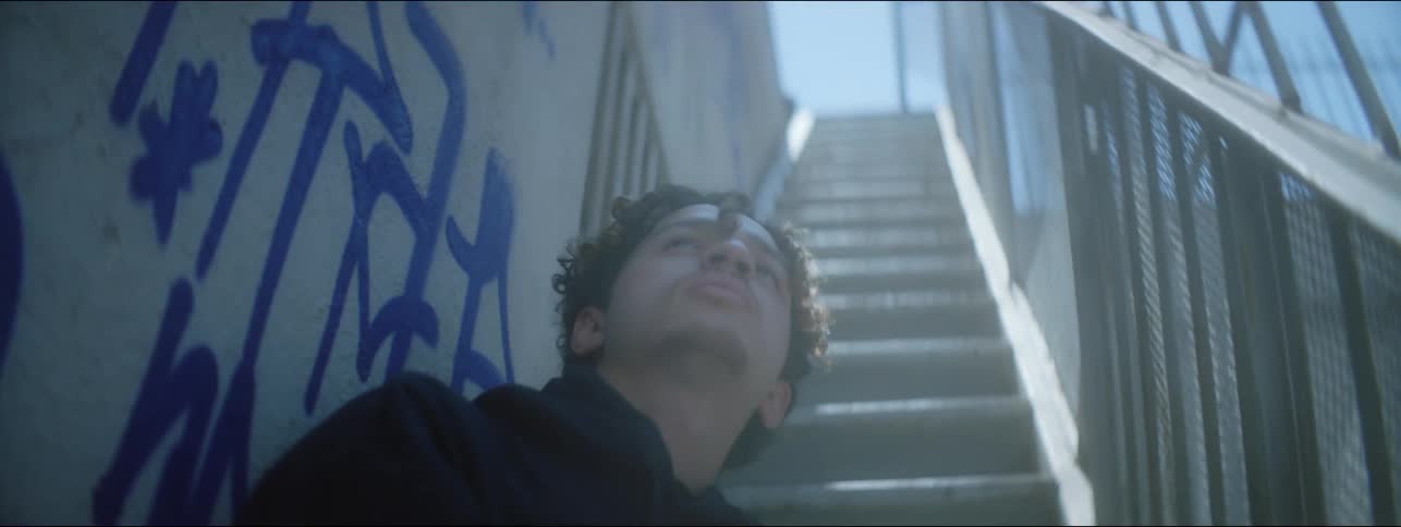 Man sits on narrow staircase near graffiti tagged wall