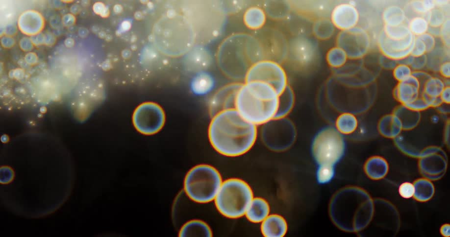 Glowing orbs of light twinkle as they move and shine as they float and fall in the darkness