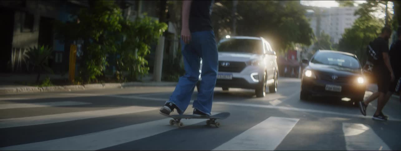Young person does skateboarding trick across crosswalk in late afternoon and looks up in amazement