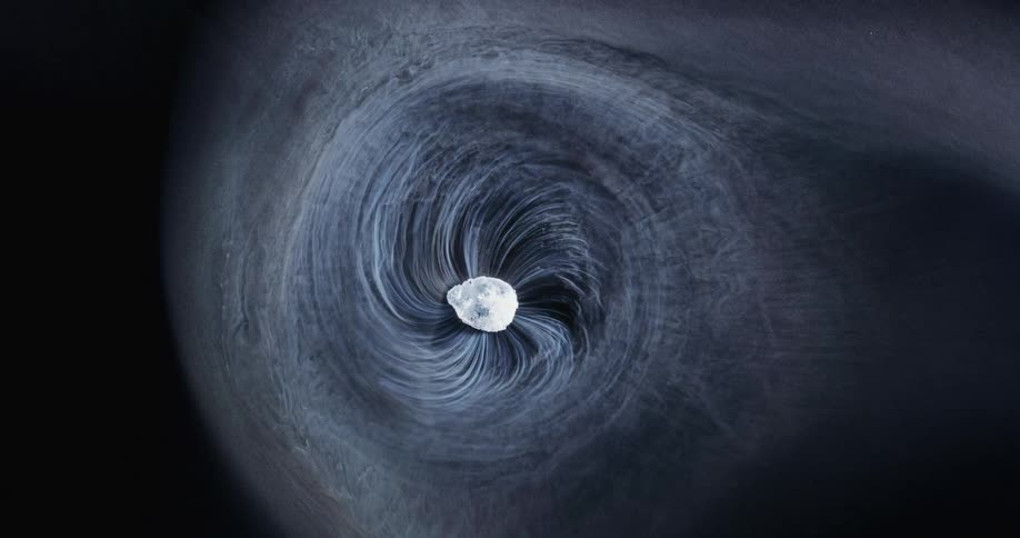 A white object turns and emits twisting wisps of smoke that spread and turn as they spread out in the darkness