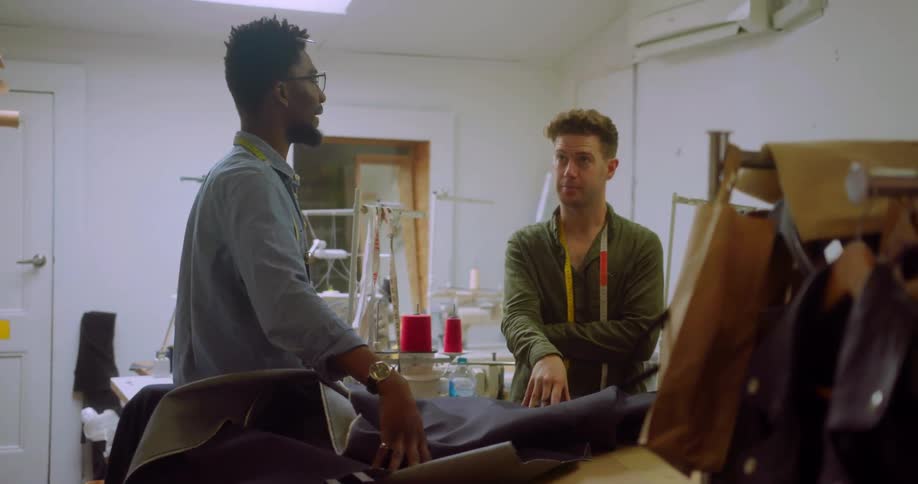Two men talk while using hand gestures by a table with cloth on it