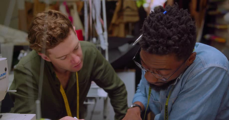 Two men lean over a table looking at a tablet and talking