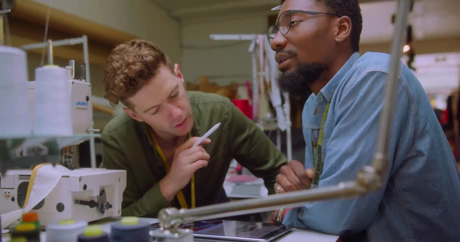 Two men using a tablet computer are talking and working in a sewing room