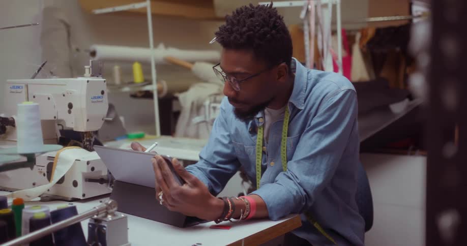 A man is using a tablet computer while he is working in a sewing room
