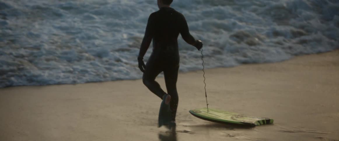 A man pulls along a surfboard towards the ocean