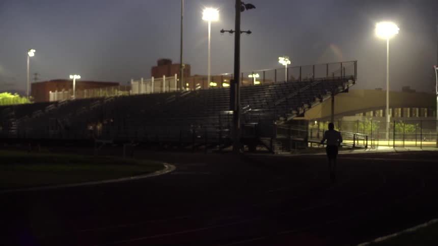 A man is running towards bleachers at night